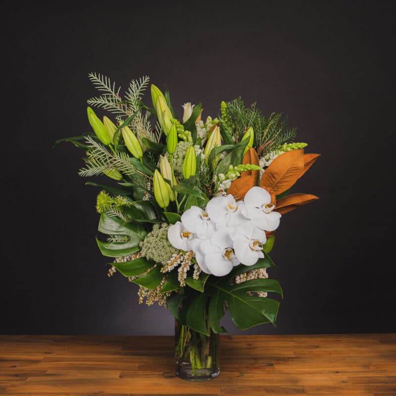 White orchids, lilies, and magnolia leaves in a glass vase. - The Village Florist Hunters Hill